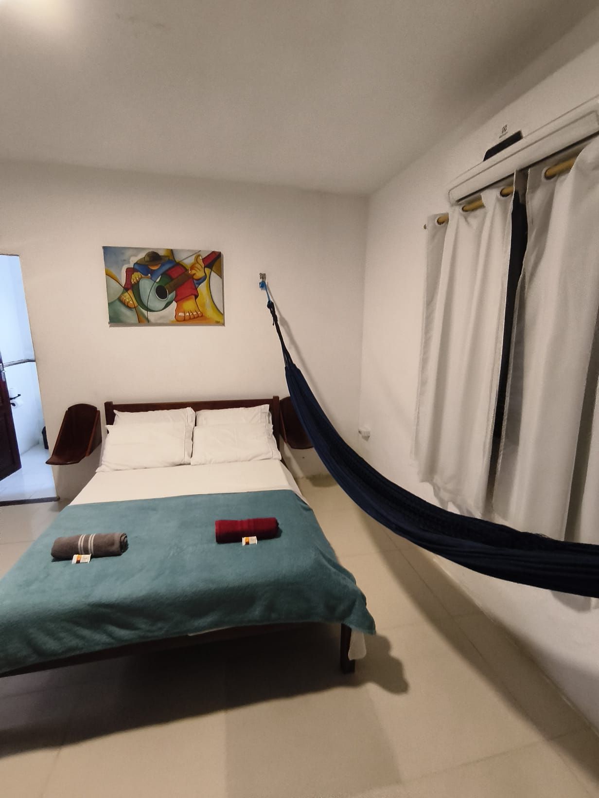 Una habitación con una cama, una hamaca, un cuadro en la pared y una cortina.
