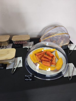 Presentación de alimentos, incluyendo mango y papaya, con etiquetas y utensilios.