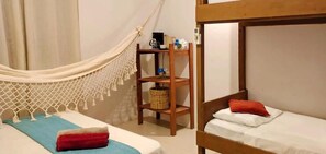 Una habitación con una hamaca, un estante con objetos y dos camas.