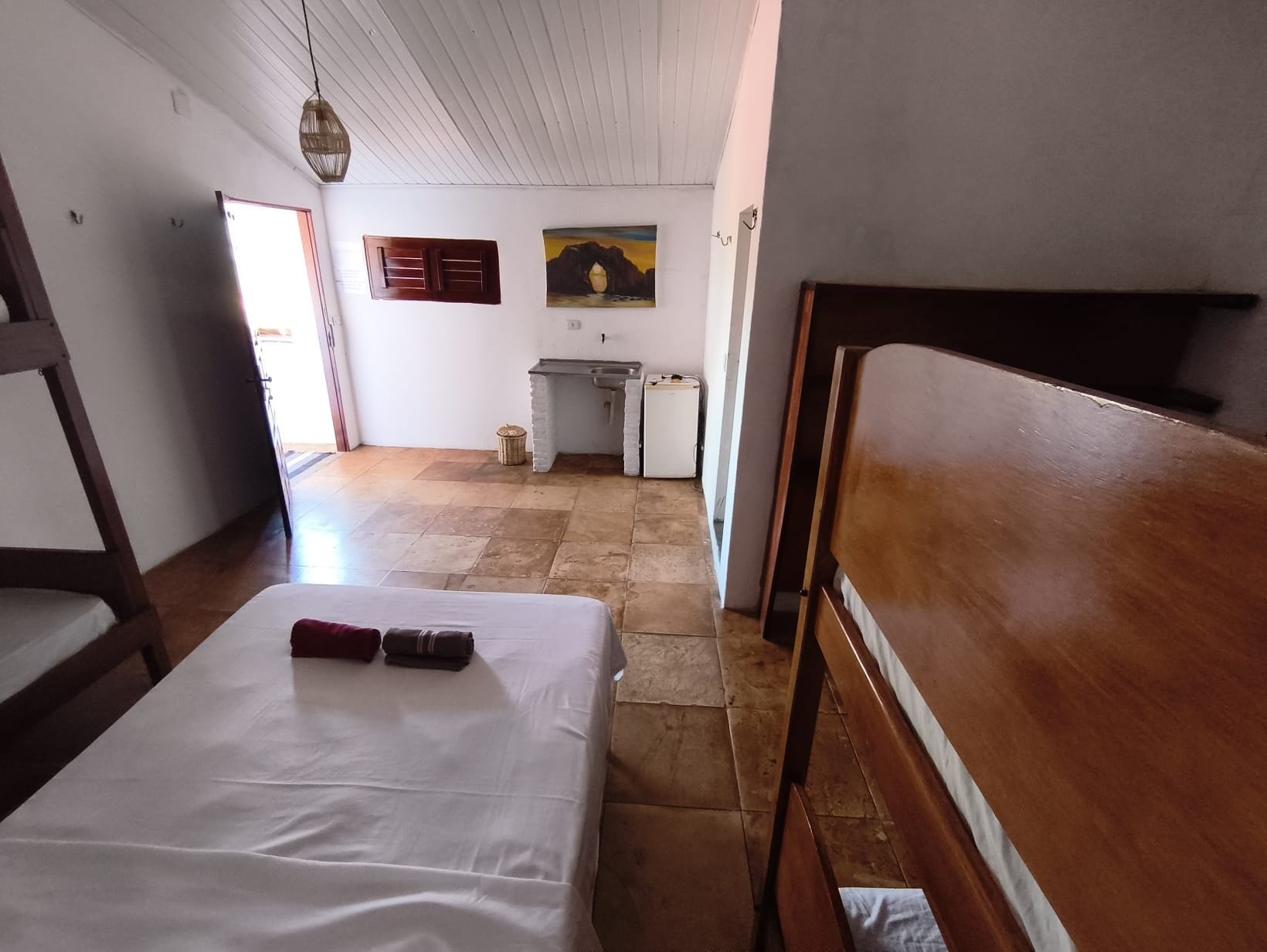 Una habitación con cama, un banco de madera, un escritorio y un refrigerador pequeño.