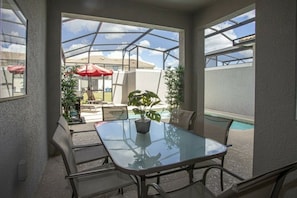 Ein Terrassenbereich im Freien mit einem Glastisch, Stühlen, einem Pool und Sonnenschirmen.