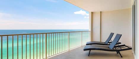Un balcón con vista al océano, dos sillones de descanso y una barandilla.