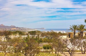 A coastal landscape with a view of the sea, mountains, and a town in the distance. - Luxury 3-Bedroom Condo | Private Rooftop | Ocean and Golf Views | Club Campestre by HCG (San José del Cabo)