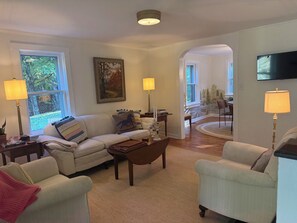 Un salon avec un canapé, des fauteuils, une table basse et un téléviseur. On y trouve également des lampes, un tableau et un tapis.