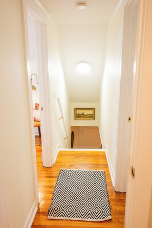 Un couloir étroit, orné d’un tapis à motifs, doté d’un plancher en bois et d’un tableau accroché au mur.