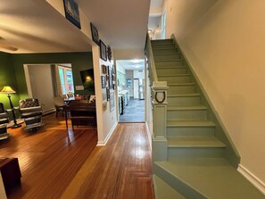A spacious hallway with a wooden floor, a staircase, and a view into a kitchen area.
