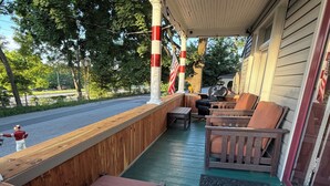 Ein überdachter Außenbereich mit Holzbänken und einem Tisch, mit Blick auf eine Straße, im Hintergrund B äume.