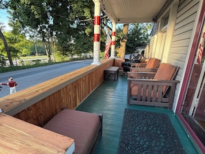 Ein überdachter Außenbereich mit Holzbänken und einem Tisch, mit Blick auf eine Straße, im Hintergrund Bäume.