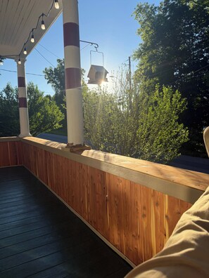 A wooden deck with a railing, a pergola with string lights, and a view of trees and sky.