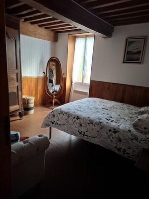 Een slaapkamer met een bed, een houten stoel, een spiegel, een raam en een deur.