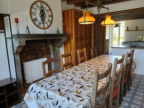 Ein Esszimmer mit einem langen Tisch, Holzsesseln, einer Uhr und einem Kamin.