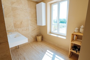 A bathroom with a white sink, a wooden floor, a window with a view, and a shelf with jars. - Land of Sharing (Saint-Bris-le-Vineux)