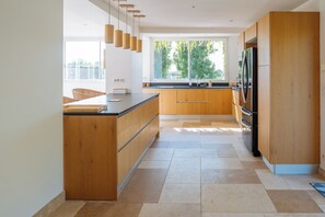 A modern kitchen with wooden cabinets, a central island, and a large window providing natural light. - Land of Sharing (Saint-Bris-le-Vineux)