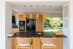 A modern kitchen with a central island, wooden cabinets, and a view of greenery outside. - Land of Sharing (Saint-Bris-le-Vineux)