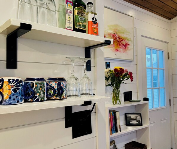 A kitchen with white cabinetry, black shelves, and a variety of kitchenware including mugs, a vase with flowers, and bottles of olive oil.