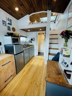 Una cocina compacta con armarios de madera, microondas integrado y refrigerador.