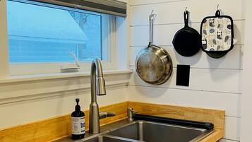 Una cocina con un lavamanos doble, encimera de madera, armarios de acero inoxidable, una ventana con persianas y utensilios de cocina colgantes.