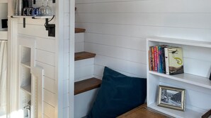 Ein Zimmer mit Holzboden, weißen Wänden, einem Bücherregal, einem gerahmten Bild und einem Fenster mit Blick.