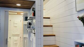 A narrow hallway with a wooden ceiling, white walls, a staircase, and a bookshelf with books.