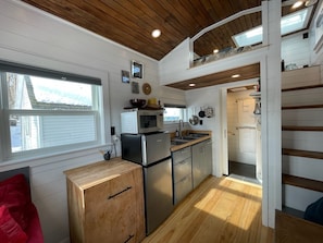 A compact kitchen with a microwave, refrigerator, and wooden cabinets.