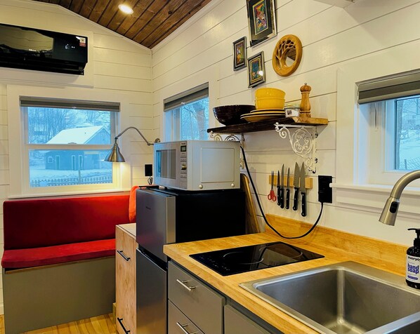 A compact kitchen with a red bench, a microwave, a sink, and a window with a view of a snowy landscape.