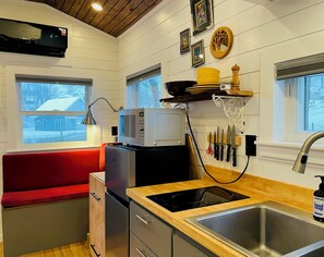 A compact kitchen with a red bench, a microwave, a sink, and a window with a view of a snowy landscape.