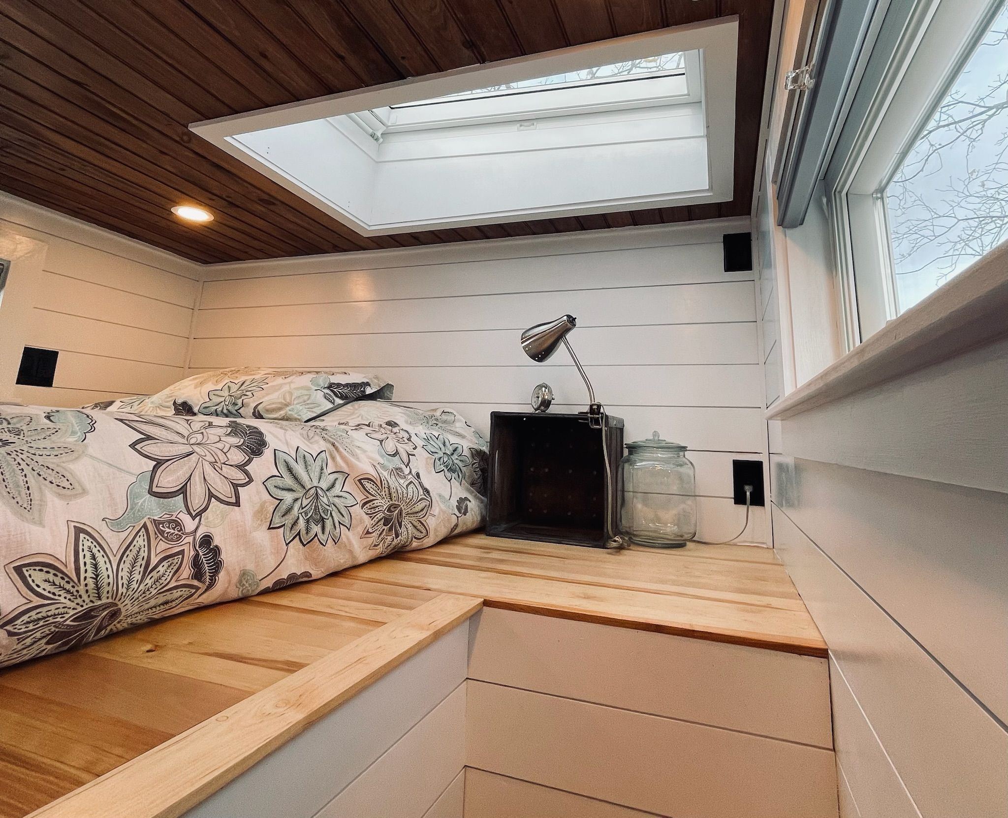 Ein Schlafzimmer mit Dachfenster, einem Bett mit floraler Bettwäsche, einem Nachttisch und einem Beistelltisch.