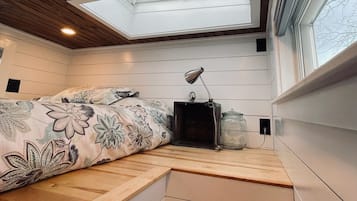 Ein Schlafzimmer mit Dachfenster, einem Bett mit floraler Bettwäsche, einem Nachttisch und einem Beistelltisch.