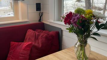 A room with a red sofa, a wooden table, a vase with flowers, and a window with a view of trees and snow.
