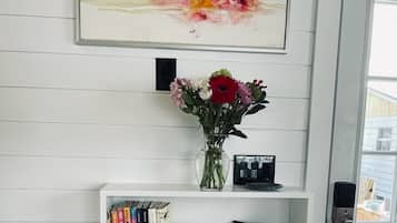 A white wall with a framed abstract painting, a vase with flowers, a bookshelf with books and a framed photo, and a door with a keypad lock.
