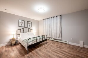 Een slaapkamer met een metalen bed, een nachtkastje met een lamp en een raam met gordijnen.