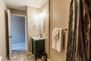 Un baño con lavamanos, espejo, toallero y una puerta que da a otra habitación.