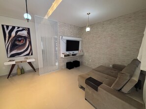 Ein modernes Wohnzimmer mit einem großen Flachbildfernseher an einer Wand mit Steinoptik, einem beigen Sofa, einem dekorativen Gemälde und einem weißen Konsolentisch.