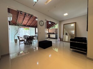 Un salón amplio con una mesa de comedor, un reposapiés negro, un espejo grande y una cocina al fondo.