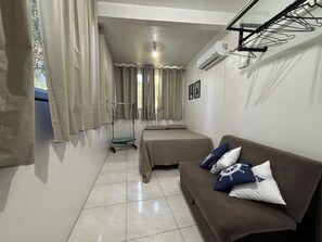 Una habitación con cama, sofá, calentador portátil y ventana con cortinas.