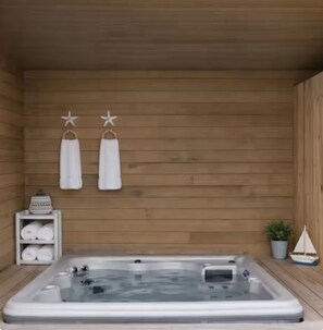 A wooden cabin with a hot tub, towels, and a small shelf with folded towels. - Sea La Vie - Hot Tub, Huge Enclosed Private Deck, Sleeps 22, Close To Town (Ocean Beach)