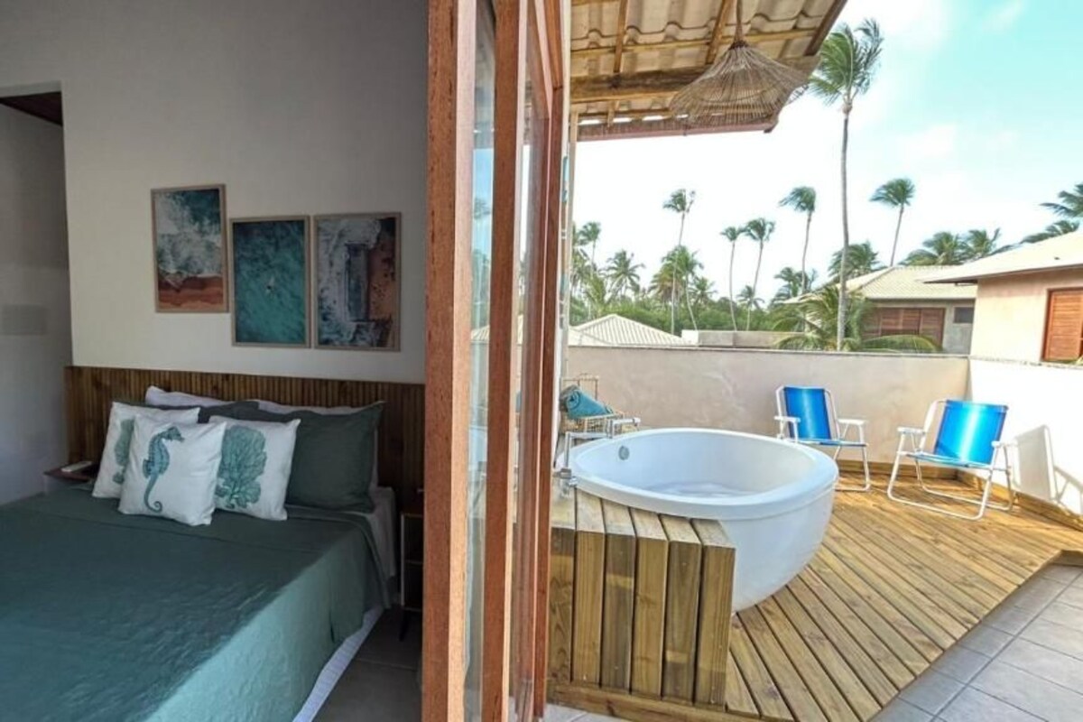 Een slaapkamer met een bed, een houten terras, een jacuzzi en uitzicht op palmbomen.