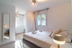 A hotel room with a bed, a bedside lamp, a window with curtains, a radiator, and a mirror. - Luxury Villa With Jacuzzi and sea Views (Nerja)