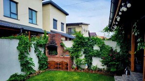 Cortile residenziale con un camino in mattoni, un prato e un muro bianco ricoperto di piante rampicanti.