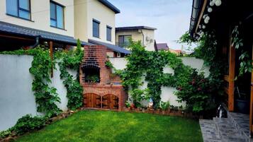 Un patio trasero residencial con chimenea de ladrillo, césped y una pared blanca cubierta de plantas trepadoras.