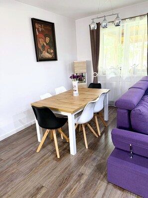 A dining area with a wooden table and chairs, a purple sofa, and a painting on the wall.