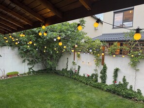 Een tuin met een houten pergola, lichtjes en een witte muur begroeid met klimplanten.
