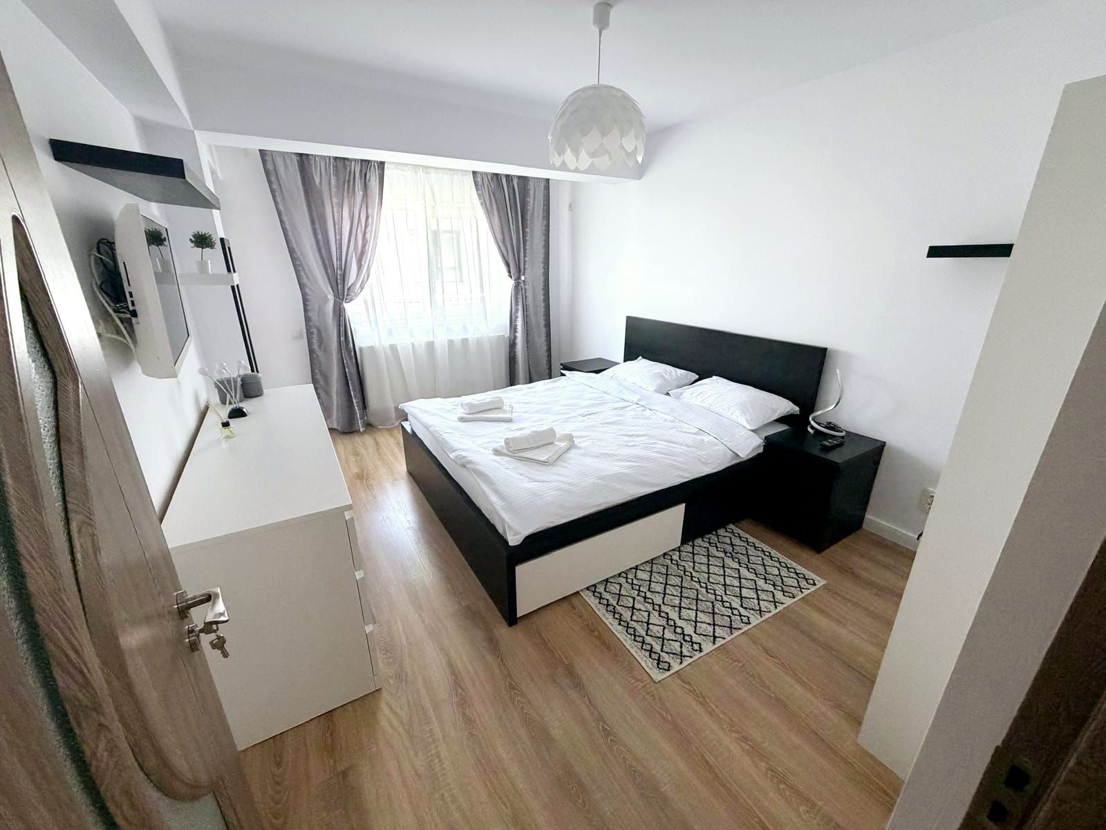 A modern bedroom with a bed, bedside tables, a desk, and a hanging light fixture.