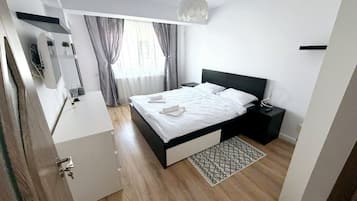 A modern bedroom with a bed, bedside tables, a desk, and a hanging light fixture.