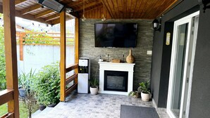 Un’area patio coperta con una televisione a schermo piatto montata a parete, un piccolo caminetto bianco e un angolo salotto con una panca e un tavolo.