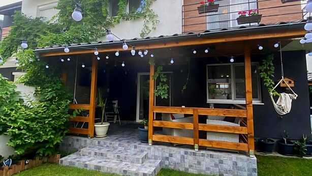 Una casa a due piani con un portico in legno, piante in vaso e luci decorative.
