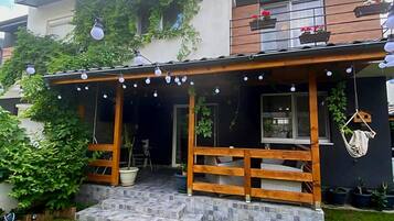 Una casa de dos pisos con un porche de madera, plantas en macetas y luces colgantes.