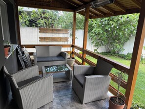 A covered outdoor seating area with wicker furniture, a glass-top table, and potted plants.
