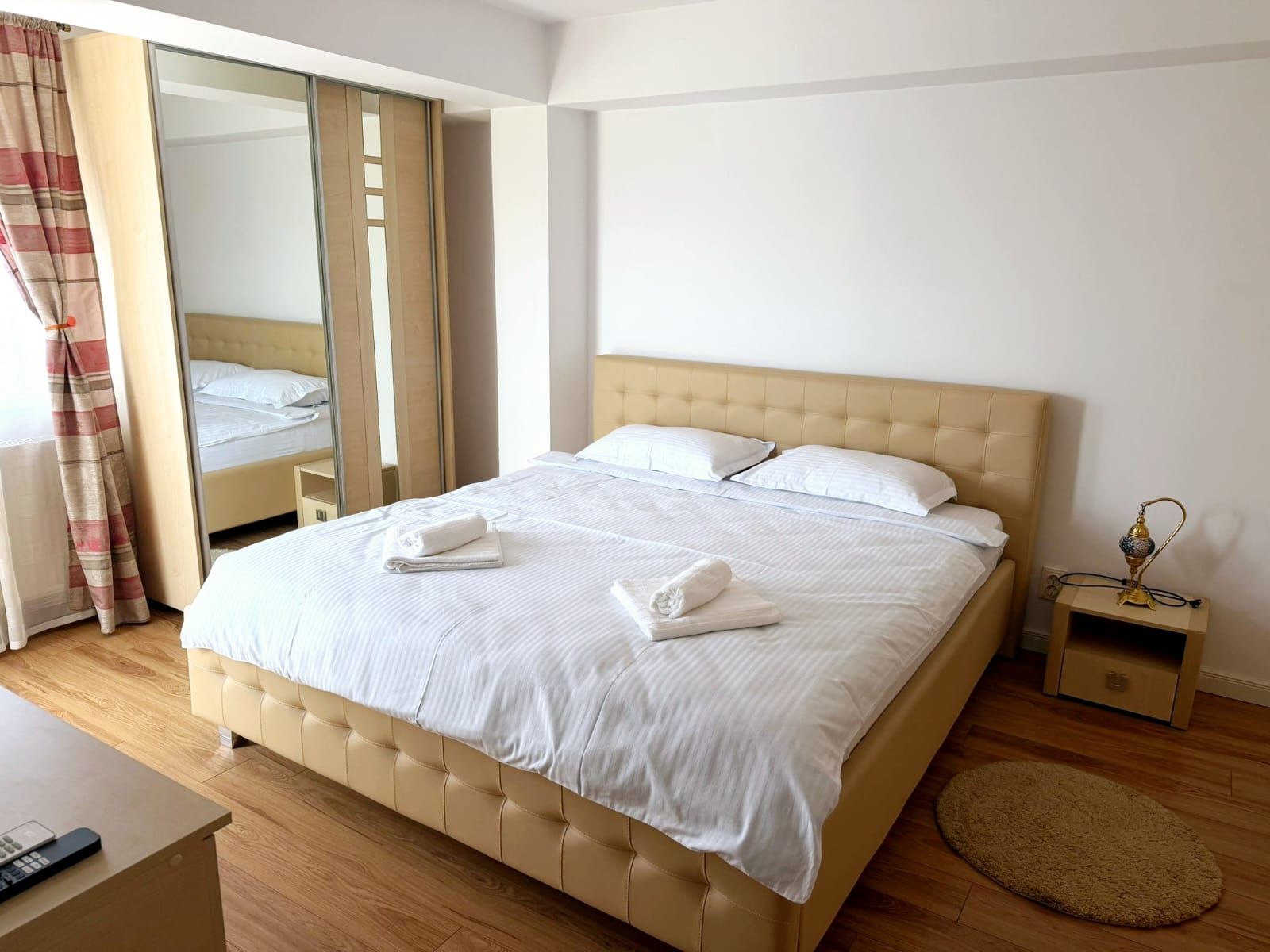 A hotel room with a large bed, a bedside table with a lamp, and a mirror.