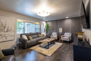 A modern living room with a sectional sofa, two armchairs, a coffee table, and a TV mounted on the wall. - 4-bedroom house with pool and hot tub.  Walking distance to downtown Spearfish. (Spearfish)